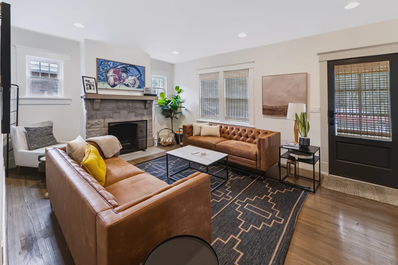 Living room with a stone fireplace, leather sofas, woven shades and a patterned rug