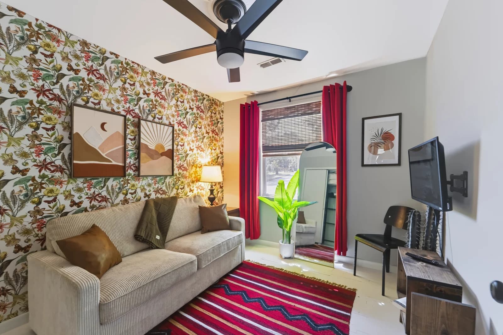 Sitting room with floral wallpaper, a gray sofa, red curtains and a full-length mirror
