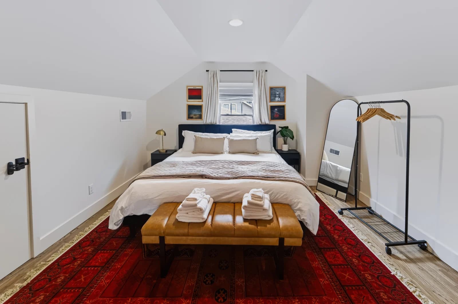 Loft bedroom with sloped ceilings, a blue headboard, leather bench and freestanding mirror