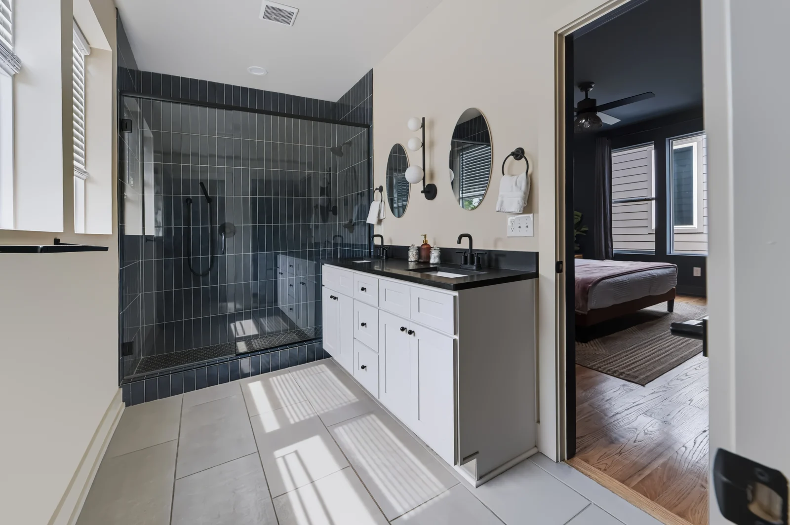 Bathroom with a tiled glass shower, white double vanity, oval mirrors and black fixtures